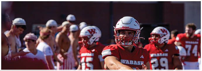 A person wearing a red football uniform with the number seven stands on a field with a crowd of people in the background and another person in a white football uniform nearby. Description generated by AI
