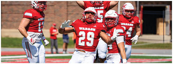 Players in red and white football uniforms are lined up on the field facing each other, preparing for a play during a game with spectators in the background. Description generated by AI