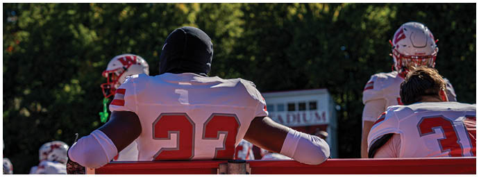 A group of people wearing white helmets with red “W" logos and red sports uniforms are huddled together on a green field. Description generated by AI