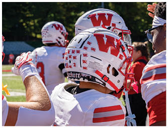 A person wearing a red football uniform with the word WABASH and the number 6 is crouched down against a partly cloudy sky. Description generated by AI