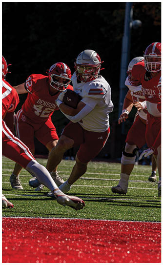 A person in a red Wabash football uniform is running on a field while holding a football, with other players and spectators visible in the background. Description generated by AI
