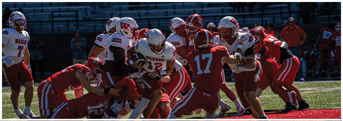 A person wearing a red football uniform with the number seven stands on a field with a crowd of people in the background and another person in a white football uniform nearby. Description generated by AI