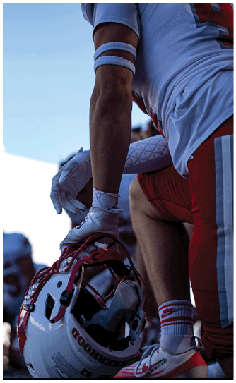 A person in a red Wabash football uniform is running on a field while holding a football, with other players and spectators visible in the background. Description generated by AI