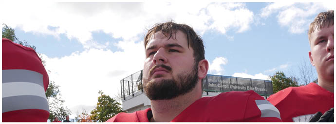 A group of people wearing white helmets with red “W" logos and red sports uniforms are huddled together on a green field. Description generated by AI