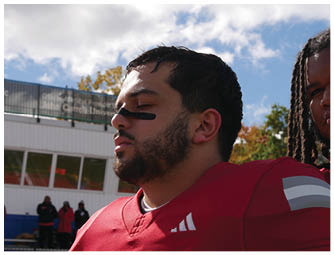 A person wearing a red football uniform with the word WABASH and the number 6 is crouched down against a partly cloudy sky. Description generated by AI