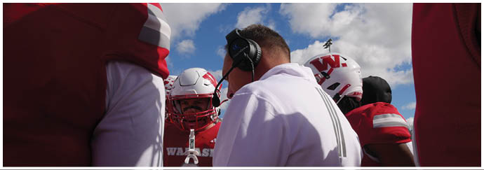 A person wearing a red football uniform with the number seven stands on a field with a crowd of people in the background and another person in a white football uniform nearby. Description generated by AI