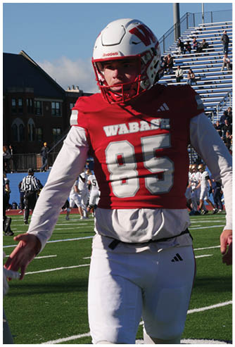 Two adults in football uniforms are jumping and reaching for the ball during a game with other players and a person in casual clothing in the background. Description generated by AI