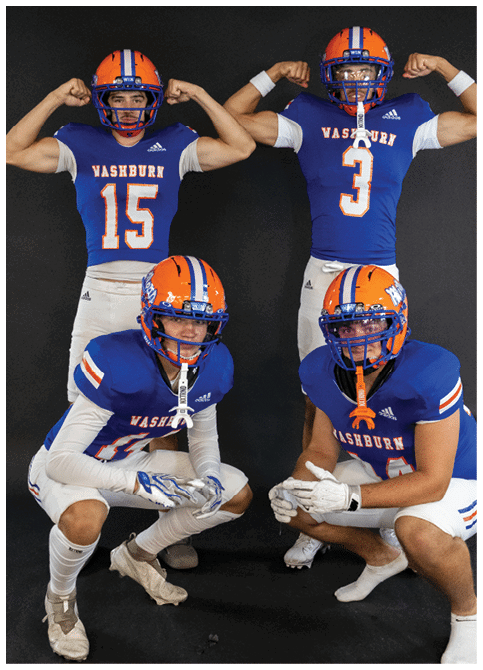 Four people wearing blue and orange football uniforms with helmets pose against a black background, two standing and flexing their arms while two crouch in front. Description generated by AI