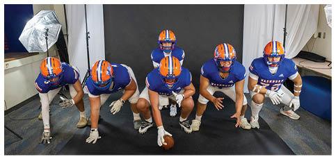 A person wearing a blue football jersey and an orange helmet with a blue faceguard is looking downward. Description generated by AI