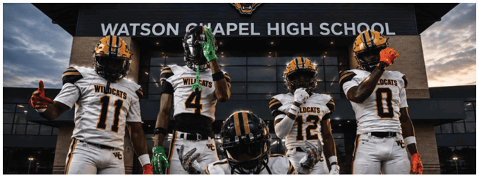 Four people in football uniforms with Wildcats logos pose in front of a building labeled Watson Chapel High School during sunset. Descripci n generada con IA