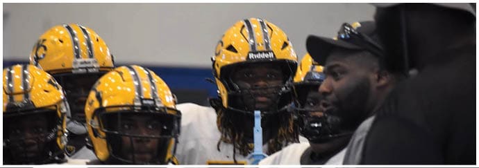 A group of people wearing yellow helmets with black stripes are gathered indoors, with two individuals in conversation. Descripci n generada con IA