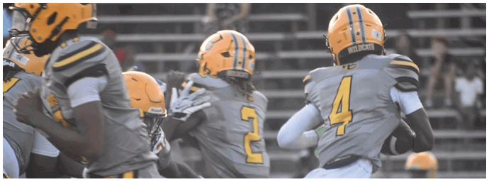 Several people wearing gray and yellow football uniforms are on a field with bleachers in the background. Descripci n generada con IA