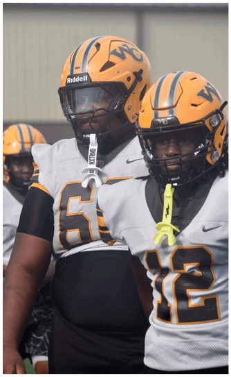 A person wearing a yellow football helmet with black stripes and a white jersey with the number 61 is standing outdoors. Descripci n generada con IA