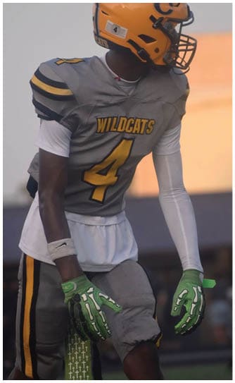A person wearing a Wildcats football uniform with the number 4 and green gloves is standing on a field. Descripci n generada con IA