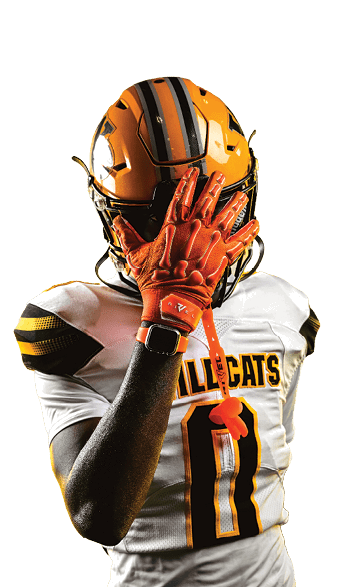 A person wearing a yellow and black football helmet and a white Wildcats jersey with the number 10 is posing with one orange-gloved hand covering their face. Descripci n generada con IA