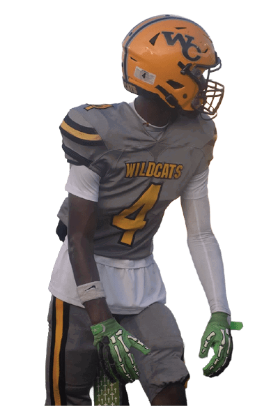 A person wearing a Wildcats football uniform with the number 4 and a yellow helmet is standing on a field, looking to the side. Descripci n generada con IA