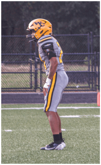 A person wearing a yellow helmet and gray football uniform is standing on a football field near the 10-yard line marker. Descripci n generada con IA