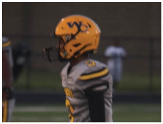 A person wearing a gray and yellow sports uniform with a white wristband is standing on a grassy field. Descripci n generada con IA