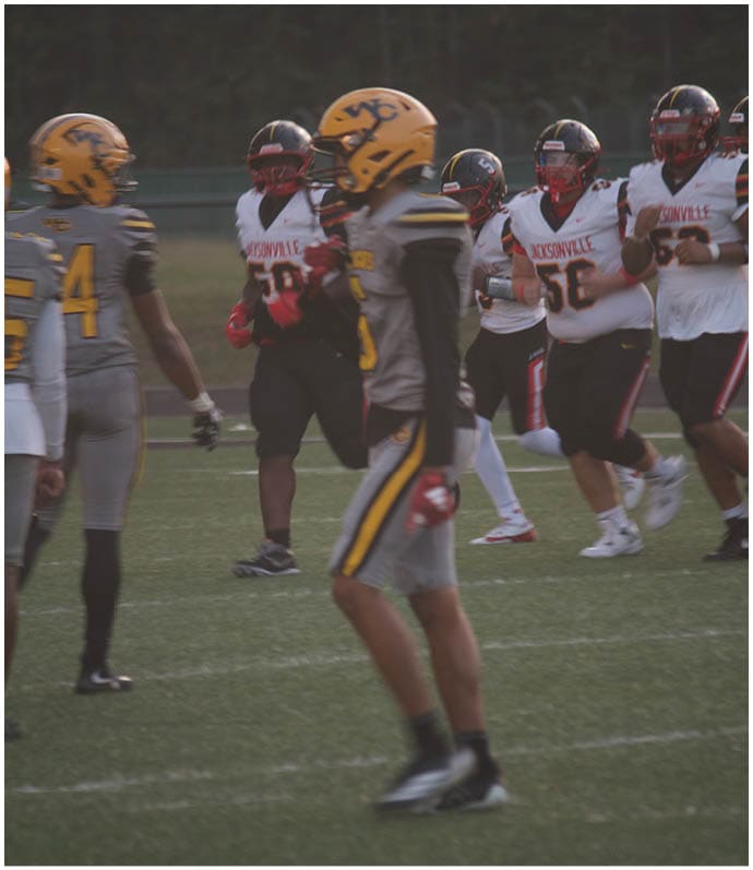 People wearing football uniforms from two different teams are standing on a field during a game or practice. Descripci n generada con IA