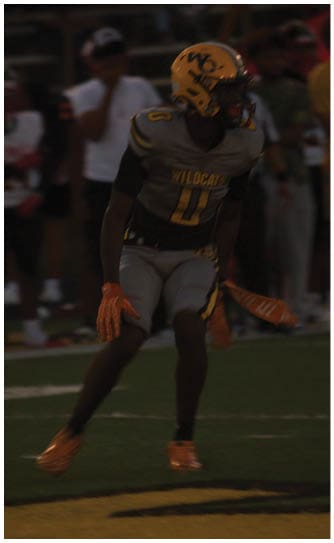 A person in a football uniform with the word Wildcats on the jersey is standing on a field during a game with spectators in the background. Descripci n generada con IA