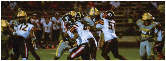 People wearing football uniforms are engaged in a play on a field under stadium lights with spectators in the background. Descripci n generada con IA