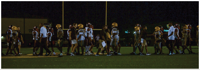 People wearing football uniforms and coaches walk across a field at night. Descripci n generada con IA