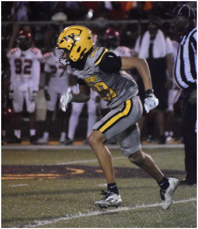 People wearing gray and yellow football uniforms are actively playing on a field, with one person holding the ball and others blocking or running. Descripci n generada con IA