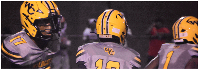Three people wearing yellow helmets and gray football uniforms with yellow numbers are on a field during a nighttime game. Descripci n generada con IA