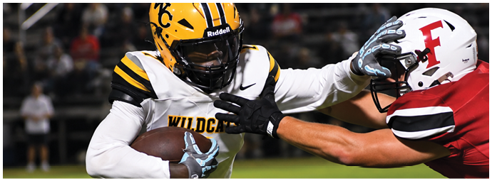 Two people in football uniforms are engaged in a play with one person holding the ball and the other reaching out to block or tackle. Descripci n generada con IA