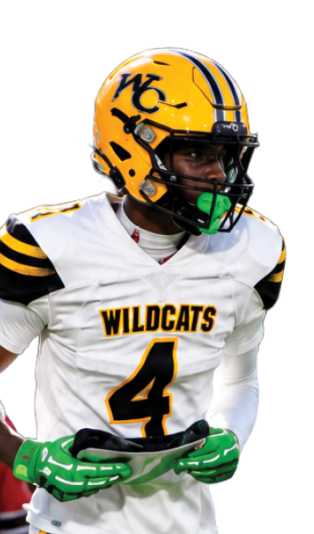 A person wearing a yellow helmet and white football uniform with “WILDCATS" on the jersey is running on a grassy field during a game. Descripci n generada con IA