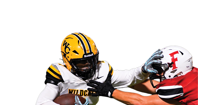 A person in a yellow and white football uniform with a helmet is running with the ball while using a stiff arm to block a person in a red and white football uniform on a grassy field. Descripci n generada con IA