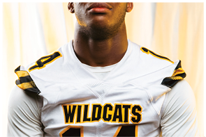 A person wearing a navy blue football jersey with white stripes on the shoulders and the words “COLLEGE PARK" printed on the front. Descripci n generada con IA