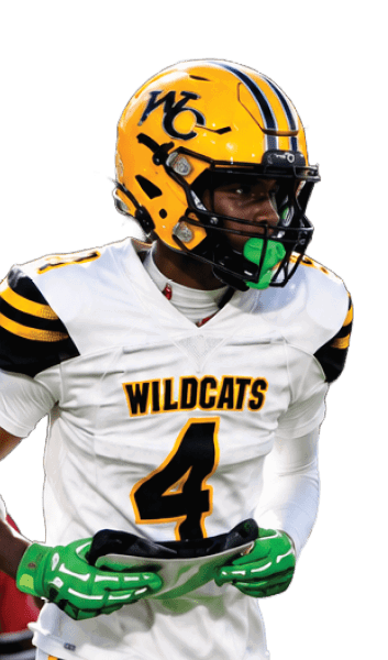 A person wearing a yellow helmet and white football uniform with “WILDCATS" on the jersey is running on a grassy field during a game. Descripci n generada con IA