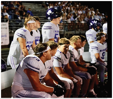 A group of football players huddled together on the field. Description generated by AI