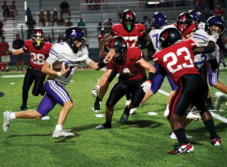 Four people wearing black football uniforms with “VISTA" on the front are standing together in a stadium with a crowd in the background, two of them holding helmets raised above their heads. Description generated by AI