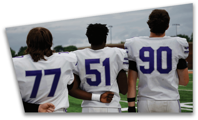 People wearing black American Canyon football uniforms and helmets are standing on a football field at night. Description generated by AI