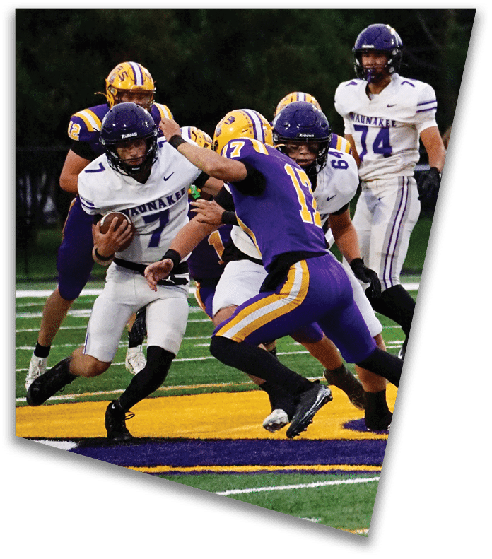 A person wearing a dark football uniform and helmet with “American Canyon" on the jersey is kneeling on one knee on a field at night. Description generated by AI