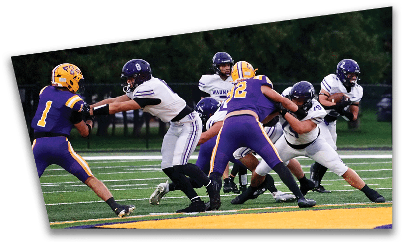 People wearing black American Canyon football uniforms and helmets are standing on a football field at night. Description generated by AI