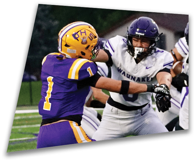 Four people in dark football uniforms and helmets stand in a row on a field, appearing focused and ready for action. Description generated by AI