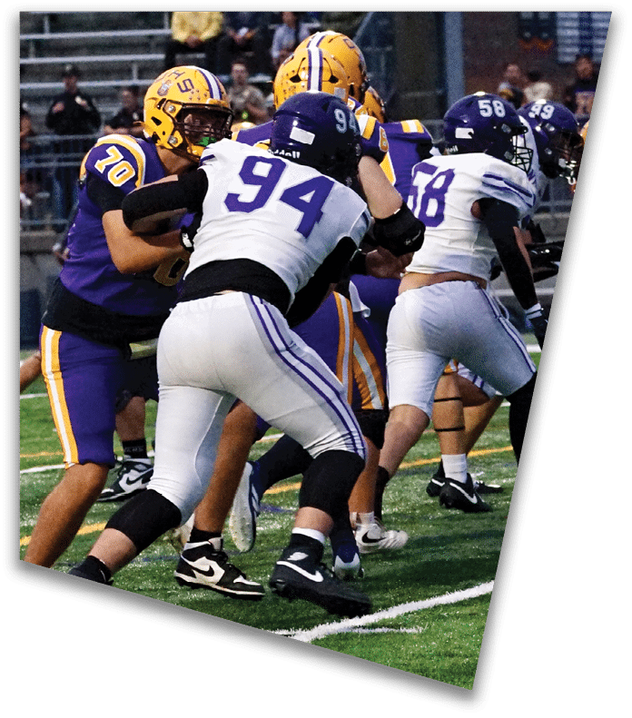 A person wearing a dark football uniform and helmet with “American Canyon" on the jersey is kneeling on one knee on a field at night. Description generated by AI
