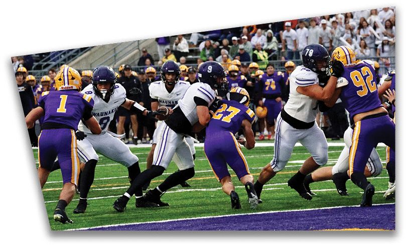 People wearing black American Canyon football uniforms and helmets are standing on a football field at night. Description generated by AI