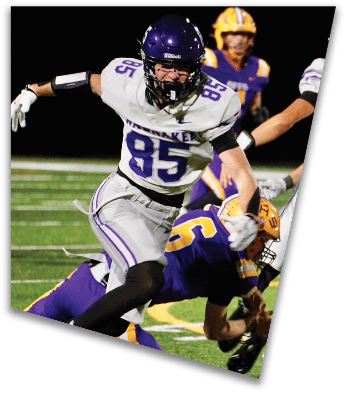 A person wearing a dark football uniform and helmet with “American Canyon" on the jersey is kneeling on one knee on a field at night. Description generated by AI