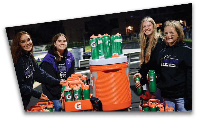 People wearing black American Canyon football uniforms and helmets are standing on a football field at night. Description generated by AI