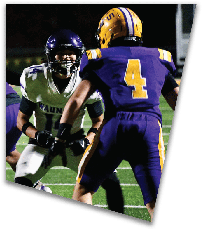 A person wearing a dark football uniform and helmet with “American Canyon" on the jersey is kneeling on one knee on a field at night. Description generated by AI