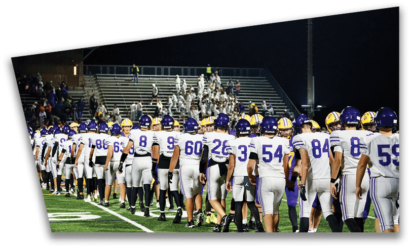 People wearing black American Canyon football uniforms and helmets are standing on a football field at night. Description generated by AI