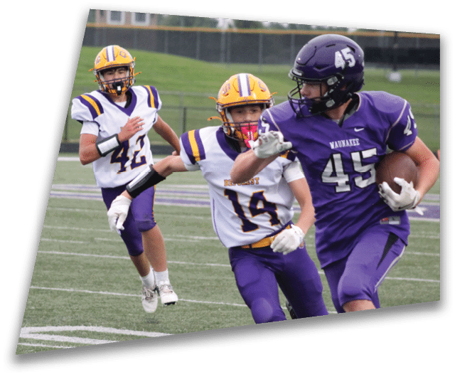 Four people in dark football uniforms and helmets stand in a row on a field, appearing focused and ready for action. Description generated by AI