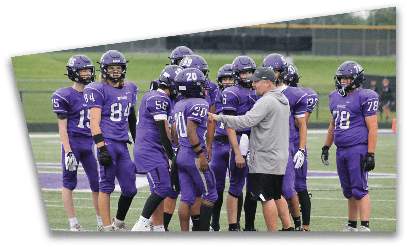 People wearing black American Canyon football uniforms and helmets are standing on a football field at night. Description generated by AI