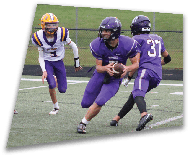 Four people in dark football uniforms and helmets stand in a row on a field, appearing focused and ready for action. Description generated by AI