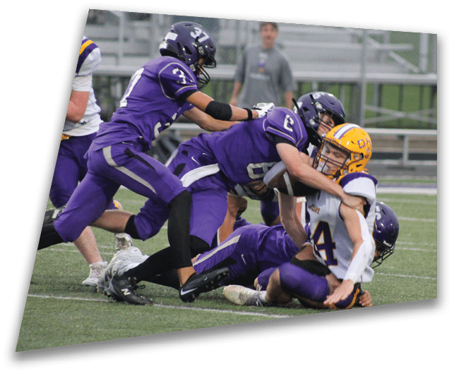 Four people in dark football uniforms and helmets stand in a row on a field, appearing focused and ready for action. Description generated by AI