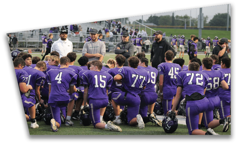People wearing black American Canyon football uniforms and helmets are standing on a football field at night. Description generated by AI
